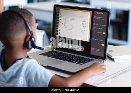 Vista posteriore di un ragazzo afro-americano che indossa le cuffie con il computer portatile e studia a casa Foto Stock