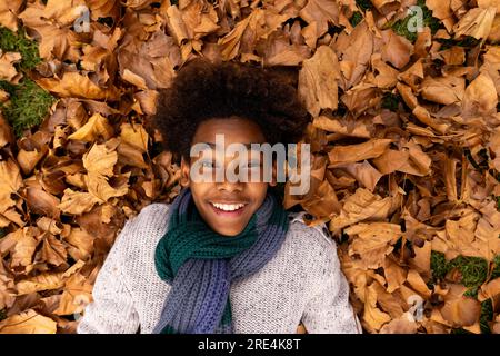 Ritratto di una felice ragazza afroamericana sdraiata in un mucchio di foglie in giardino Foto Stock