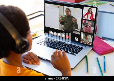 Un ragazzo birazziale che ha una videoconferenza con un insegnante maschio e studenti diversi su un computer portatile Foto Stock