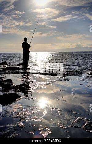 Un pescatore nell'Abisso di Chigogafuchi sull'isola di Enoshima, Kanagawa, Giappone, di fronte al tramonto del sole in solitudine Foto Stock