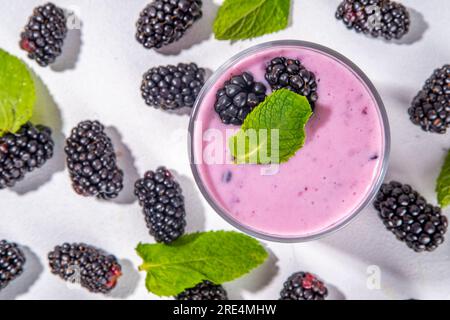 Due bicchieri di frullato blackberry, yogurt o frullato con bacche fresche e foglie di menta su sfondo bianco del tavolo Foto Stock