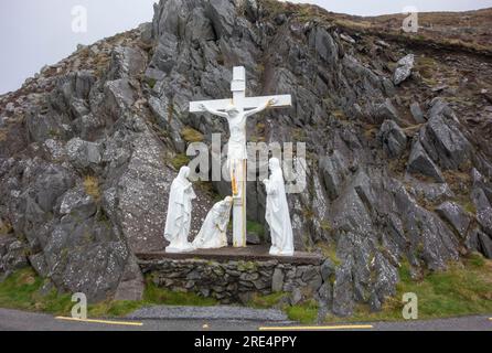 Crocifisso e alcune statue di fronte a una formazione rocciosa vicino a Dingle, una città in Irlanda Foto Stock