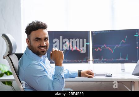 Felice e sorridente trader indiano o broker azionario guardando la macchina fotografica in ufficio - concetto di successo, trading online e fiducia. Foto Stock