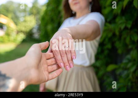 Donna con fidanzamento o anello nuziale sulla sua mano. Il suo partner che gli tiene la mano. Donna sorridente e felice Foto Stock