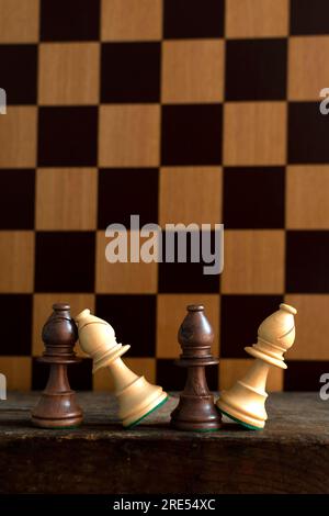 Le pedine degli scacchi sono elegantemente posizionate su un tavolo di legno con una scacchiera sullo sfondo, che mostra strategia e competizione Foto Stock