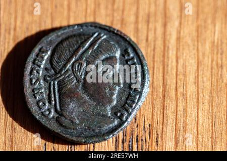 Antica moneta romana dedicata a Costantino I.. Manufatto artistico di epoca romana. Manufatto storico su sfondo ligneo. Oggetto da collezione Foto Stock
