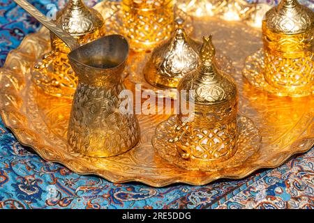 Set di caffè turco orientale dorato su un tappeto a motivi blu Foto Stock