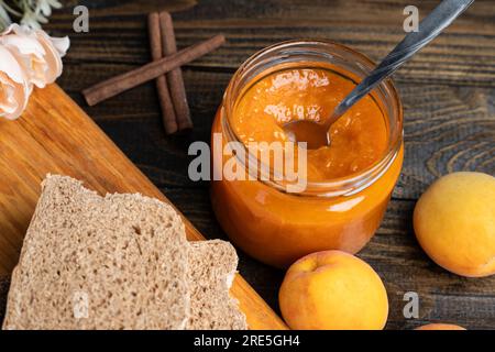 Marmellata di albicocche in vaso di vetro, pane e albicocche fresche su fondo di legno Foto Stock