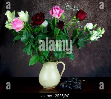 Fiori assortiti in una caraffa di vino in ceramica con uva su una superficie di legno lucidato Foto Stock