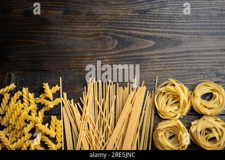 Forme di pasta, spaghetti, fusilli, tagliatelle, ingredienti della cucina italiana su uno sfondo di legno Foto Stock