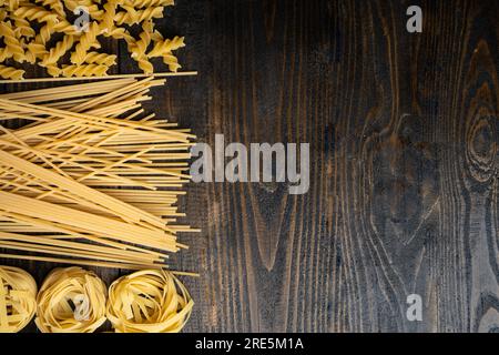 Forme di pasta, spaghetti, fusilli, tagliatelle, ingredienti della cucina italiana su uno sfondo di legno Foto Stock