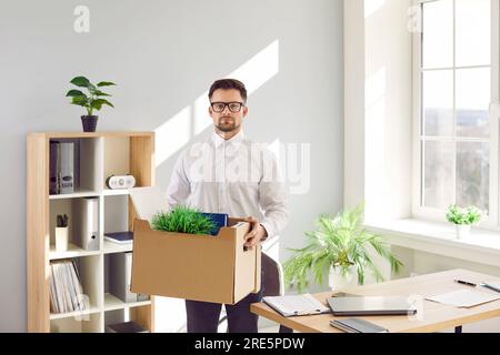 Un giovane lavoratore d'ufficio che lascia o viene licenziato confeziona la sua roba e lascia il posto di lavoro Foto Stock