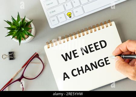 Frase scritta a mano abbiamo bisogno di un cambiamento in blocco note, ambiente Office, tastiera del computer, occhiali da lettura, graffette, Bel background da ufficio, Mot Foto Stock