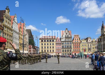 Vista esterna soleggiata, gruppo di soldati sfilano nella piazza del mercato di Wrocław, circondata da un vecchio edificio colorato a Breslavia, Polonia. Foto Stock