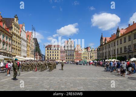 Vista esterna soleggiata, gruppo di soldati sfilano nella piazza del mercato di Wrocław, circondata da un vecchio edificio colorato a Breslavia, Polonia. Foto Stock