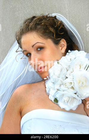 Bella giovane sposa tiene il suo bouquet vicino al viso. È solenne e scintilla sui suoi fiori alla telecamera. Foto Stock