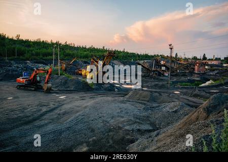 Escavatori e dumper che lavorano sul movimento terra in miniere a cielo aperto negli impianti minerari e di lavorazione. Foto Stock