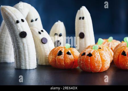 Halloween carino zucca arancia frutta e spaventoso banana fantasmi mostri con volti al cioccolato. Sano spuntino da dessert con volti divertenti per la festa dei bambini Foto Stock