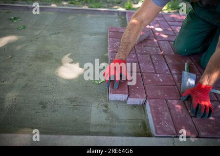 Un lavoratore poggia pietre di pavimentazione rosse su una superficie preparata in modo uniforme. Foto Stock