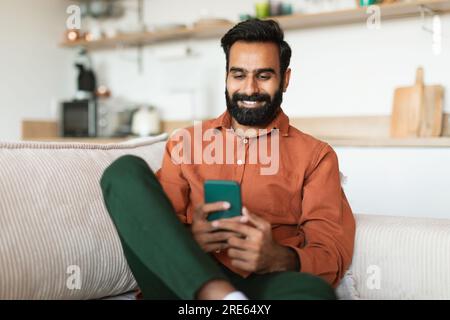 Uomo arabo che usa gadget per telefoni cellulari per comunicare a casa Foto Stock