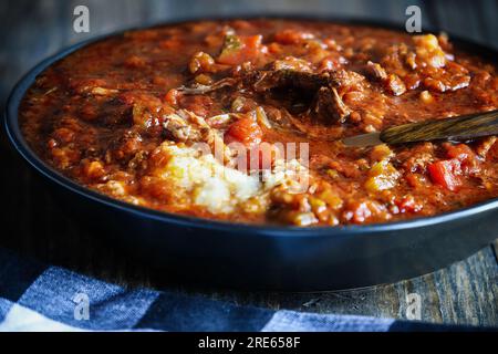 Abbondante ciotola di ragù di manzo fresco fatto in casa su polenta. Profondità di campo estremamente bassa con sfondo e primo piano sfocato. Foto Stock