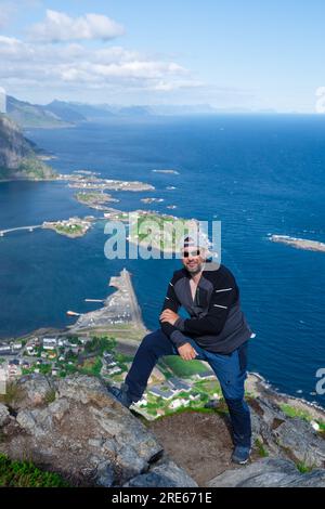 Rilassato e felice escursionista gode di una vista mozzafiato sulle cime di Reinebringen delle isole Lofoten, dei fiordi e della Norvegia Foto Stock