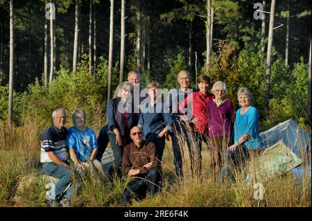 Mamma di quasi 100 anni, sta orgogliosamente tra i suoi figli e suoceri. Sono in piedi e seduti in un ambiente rustico di foresta e metallo rovesciato Foto Stock