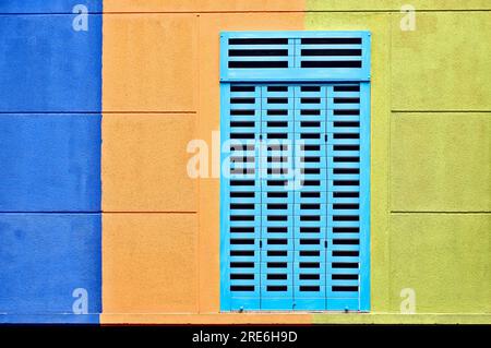 Una finestra chiusa con persiane blu su una parete blu, arancione e verde Foto Stock