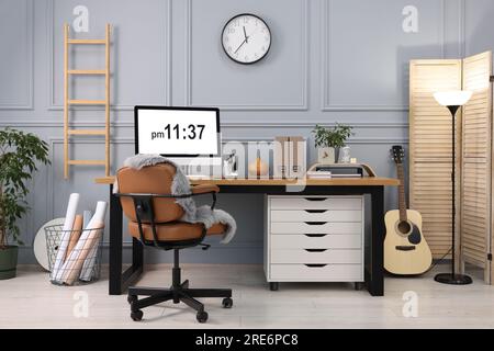 Elegante ambiente di lavoro con computer, piante domestiche e cancelleria su una scrivania di legno vicino a una parete grigia a casa Foto Stock