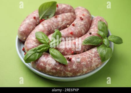 Salsicce crude fatte in casa, foglie di basilico e grani di pepe su tavola verde, primo piano Foto Stock