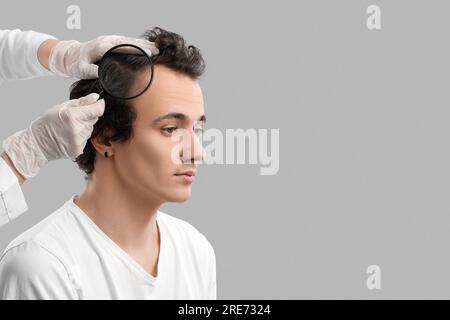 Medico che esamina giovane uomo con problemi di perdita di capelli su sfondo grigio Foto Stock