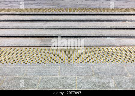 ampia e moderna scalinata in pietra con pavimentazione tattile antiscivolo gialla per la comodità dei pedoni Foto Stock