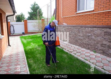 Un uomo lavora in giardino, spruzzando le erbacce da uno spruzzatore. Foto Stock