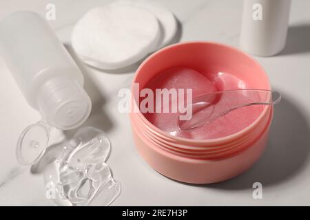 Barattolo di cerotti sotto gli occhi con cucchiaio e prodotti cosmetici su un tavolo in marmo bianco, primo piano Foto Stock