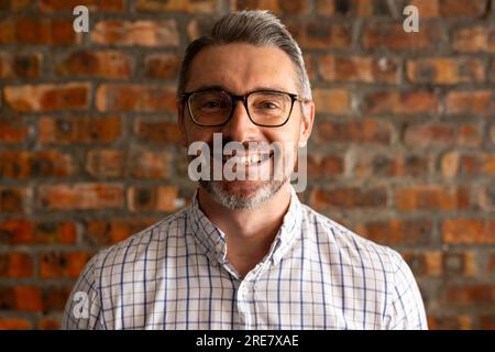 Ritratto di un uomo d'affari caucasico sorridente contro un muro di mattoni in un ufficio moderno Foto Stock