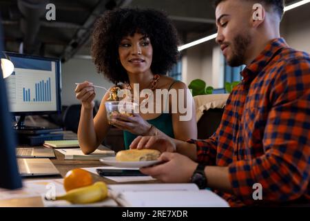 Un uomo e una donna felici e diversificati che fanno uno spuntino insieme in ufficio Foto Stock