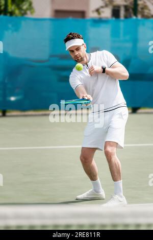pallina da tennis rimbalzante, bel tennista che si pratica sul campo, tenendo racchetta, sport e tempo libero Foto Stock