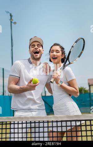 uomo eccitato e donna felice che tiene palla da tennis e racchetta, estate, sport di coppia e tempo libero Foto Stock