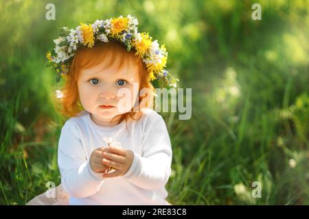 Una bambina carina indossa una bella corona di primavera all'aperto Foto Stock