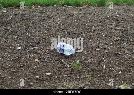 Una foto ravvicinata di una piccola bottiglia d'acqua su un terreno pieno di corteccia. Foto Stock