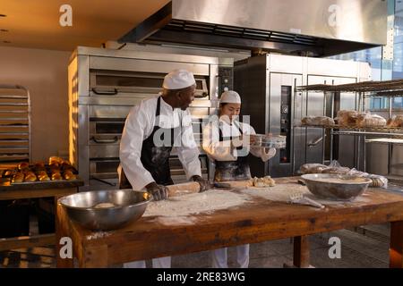 Allegri diversi panettieri che indossano grembiuli nella cucina del panificio e preparano l'impasto Foto Stock