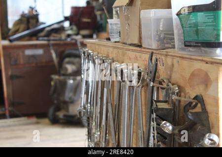 Una foto ravvicinata di una fila di chiavi, chiavi e altre attrezzature appese a un armadietto di legno in un'officina. Foto Stock