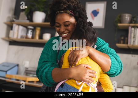 Felice madre e figlia afroamericana che si abbracciano in cucina a casa Foto Stock