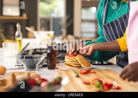 La parte centrale della madre e della figlia afro-americana prepara pancake in cucina a casa Foto Stock