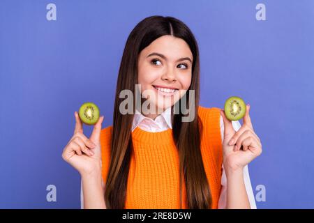 Ritratto di una ragazza dalla mentalità carina sorridente che regge due kiwi sembrano spazi vuoti isolati su sfondo di colore viola Foto Stock