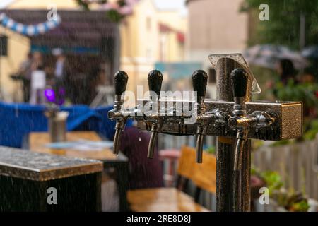 Rubinetti cromati per birra alla spina in un caffè di strada sotto la pioggia. Dettaglio della macchina per la birra, dispenser per la birra, primo piano, messa a fuoco selettiva, stile retrò Foto Stock