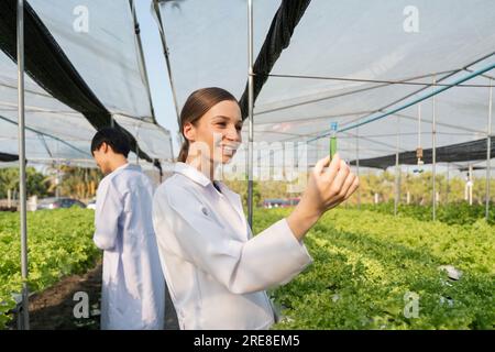 Biologi donna e uomo che esaminano la qualità dell'acqua e controllano i batteri nell'acqua dei fertilizzanti nell'orto idroponico della serra Foto Stock