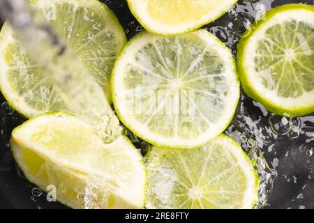 Primo piano di limoni e limoni tagliati in acqua con spazio per la copia su sfondo nero Foto Stock