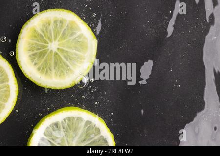 Primo piano delle fette di lime e limone in acqua con spazio di copia su sfondo nero Foto Stock