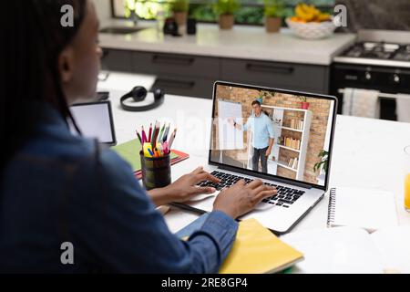 Vista posteriore di una studentessa afroamericana che sta effettuando una videochiamata con un insegnante maschio sul computer portatile Foto Stock